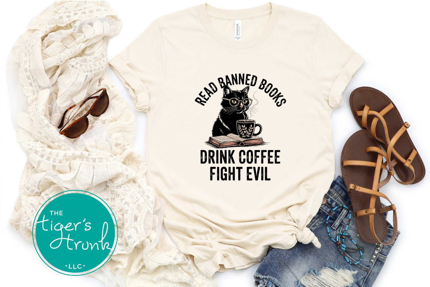 Beige t-shirt with a cat graphic and text, paired with sunglasses, scarf, and sandals on a white background.