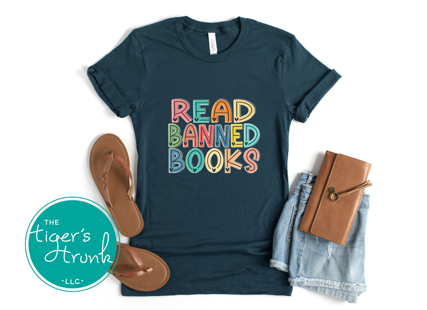 Navy t-shirt with 'Read Banned Books' text, sandals, denim shorts, and a brown notebook on a white background.