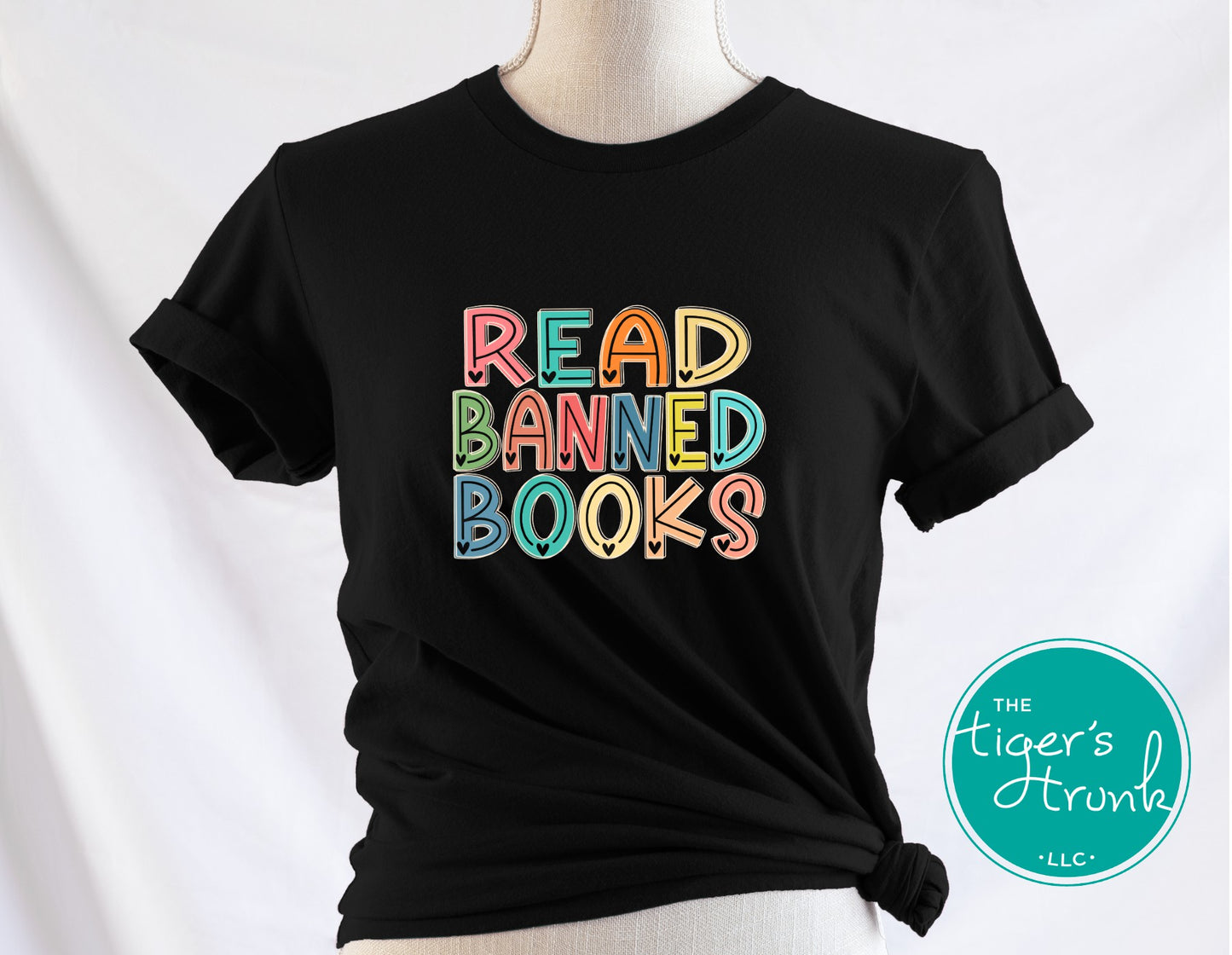 Black t-shirt with colorful 'Read Banned Books' text on a mannequin against a white background, featuring the brand 'The Tiger's Trunk'.
