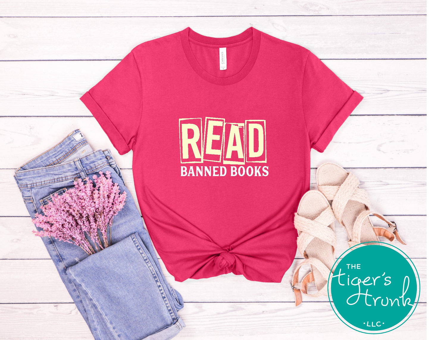 Pink t-shirt with 'READ BANNED BOOKS' text on a wooden surface with jeans and flowers.