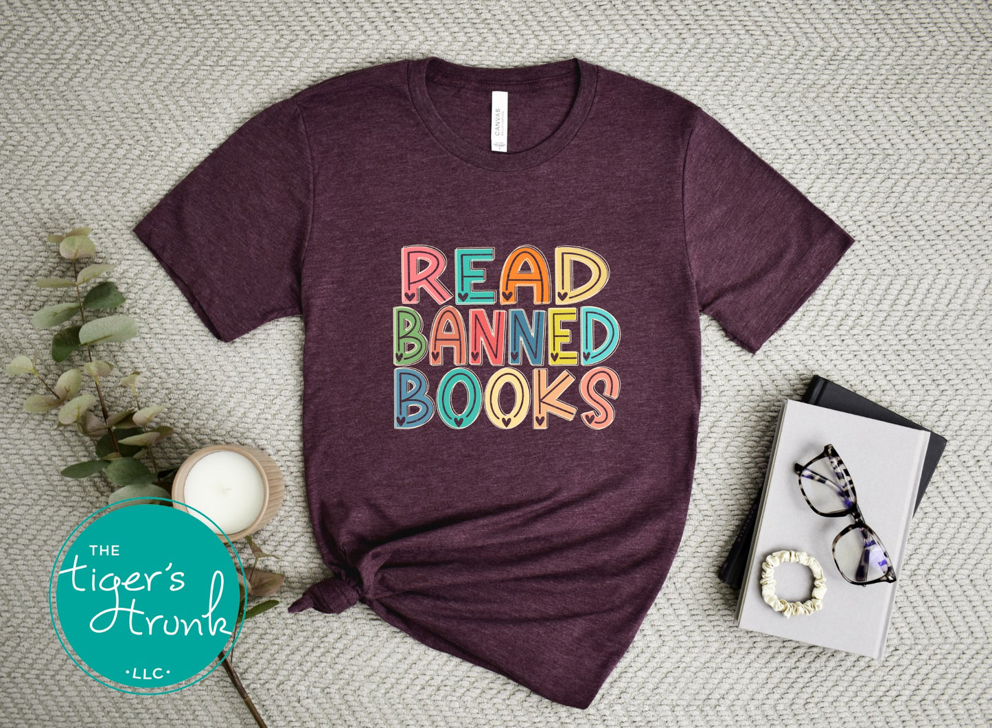 Maroon t-shirt with 'Read Banned Books' text on a textured surface with decor items.