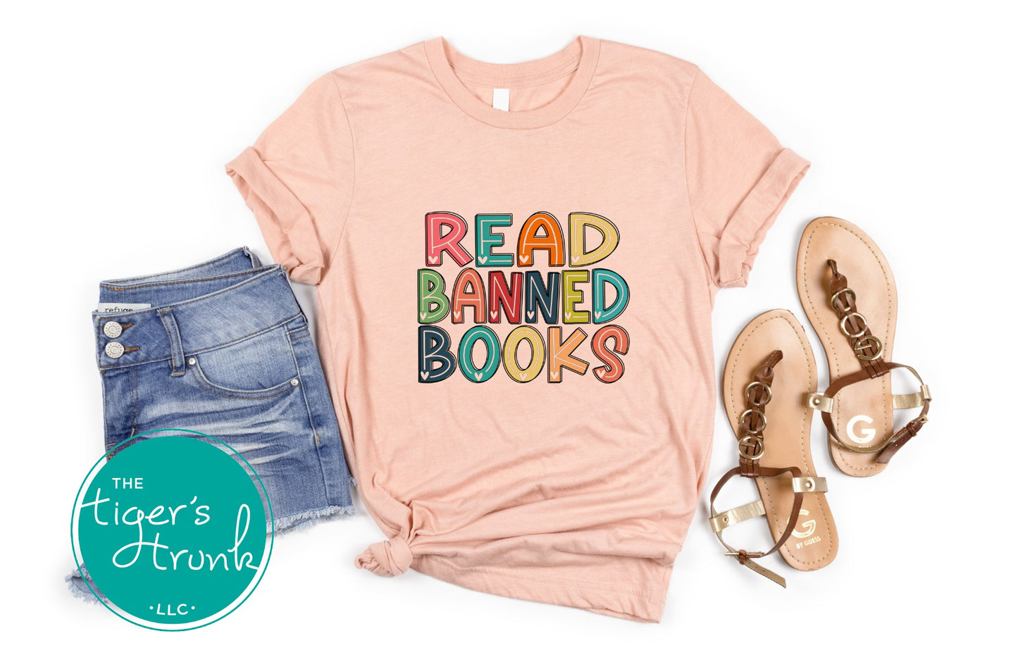 Pink t-shirt with 'READ BANNED BOOKS' text, denim shorts, and sandals on a white background.