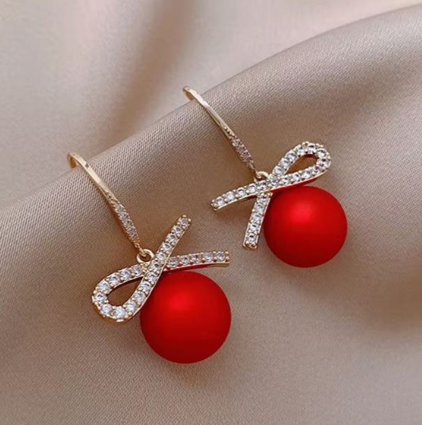 pair of red bauble earrings with rhinestone bow knot detail on soft beige fabric