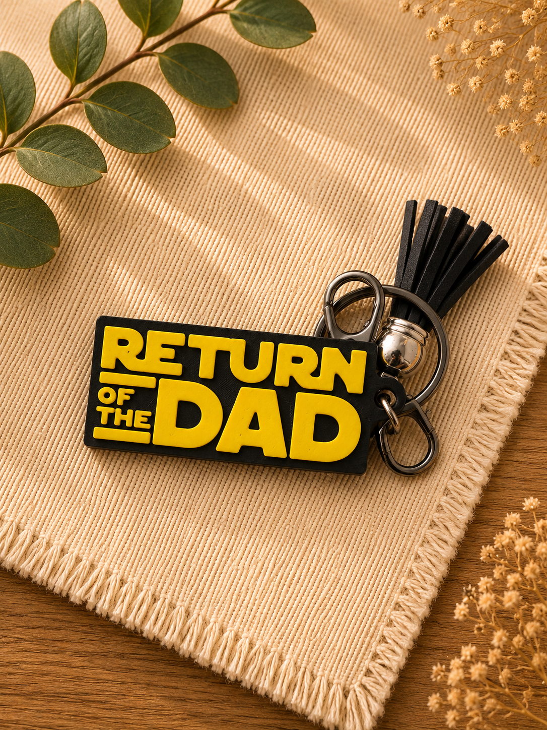 Funny Return of the Dad sci-fi inspired keychain with black tassel and lobster clasp displayed beside greenery and dried florals