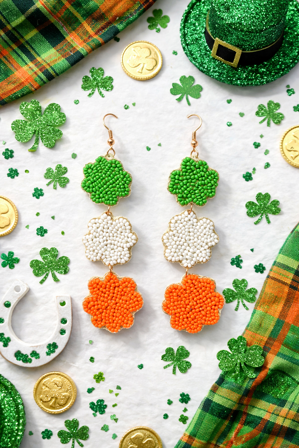 Flat lay of triple shamrock green white and orange beaded St. Patrick’s Day dangle earrings with festive Irish decorations