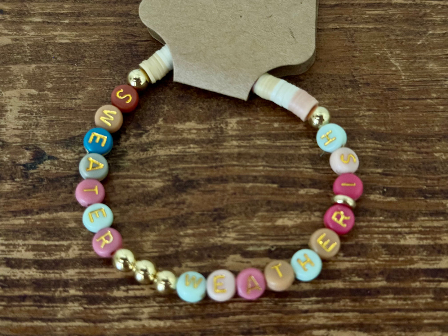 Colorful beaded bracelet with letter beads spelling 'SWEATER' on a wooden surface