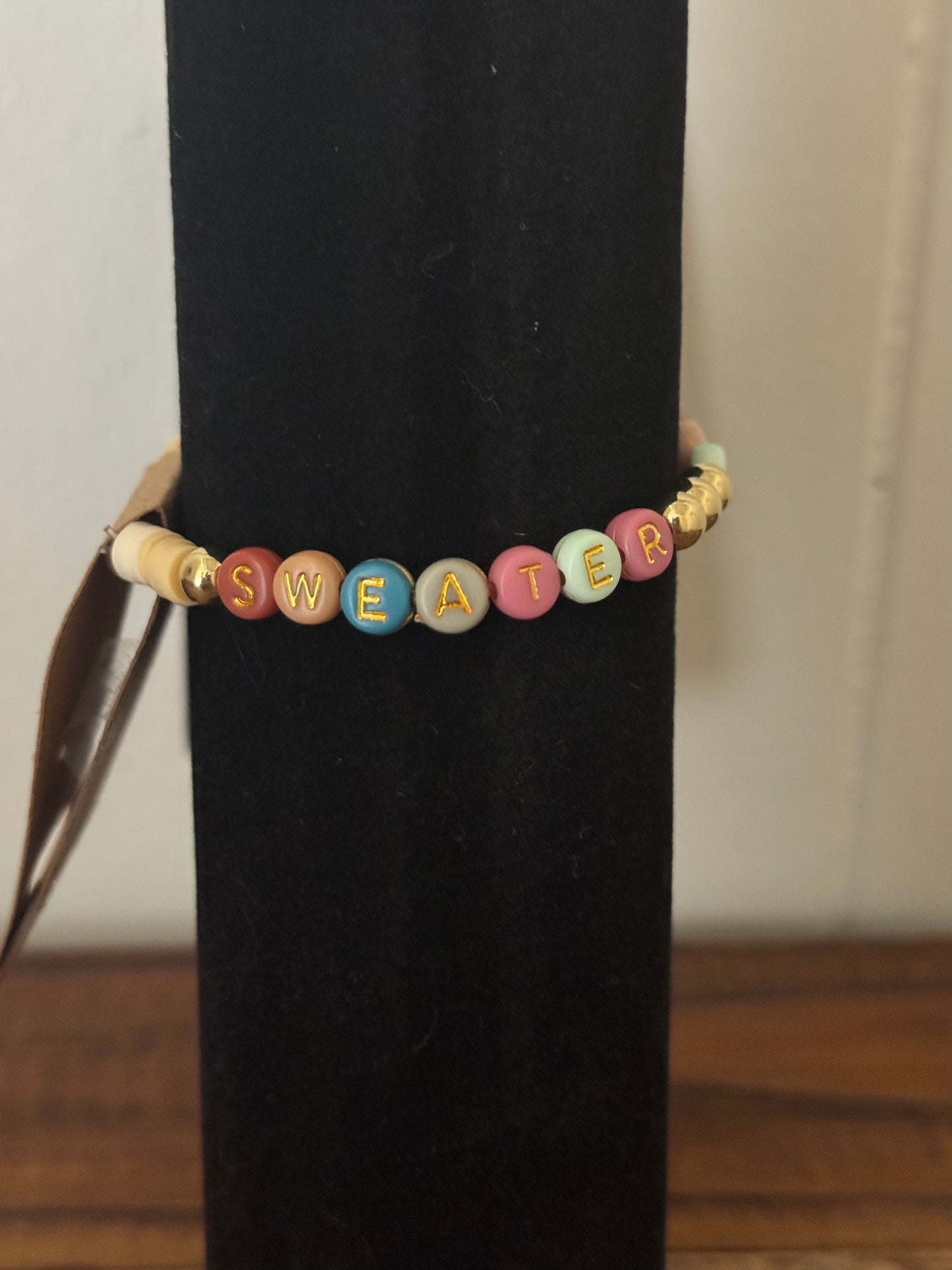 Bracelet with colorful beads spelling 'SWEATER' on a black background