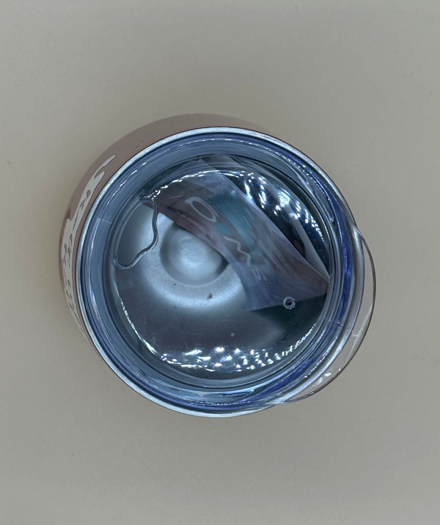 Close-up of a metallic container with a clear lid on a beige background