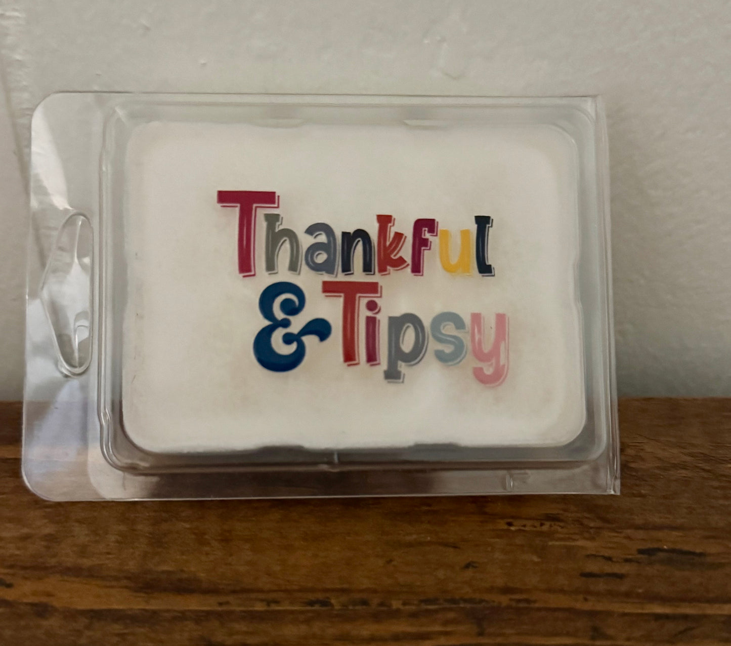 Wax melt in packaging with 'Thankful & Tipsy' text on a wooden surface.