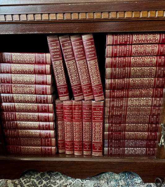 Stack of wrapped presents with a card on a wooden floor next to a bookshelf.