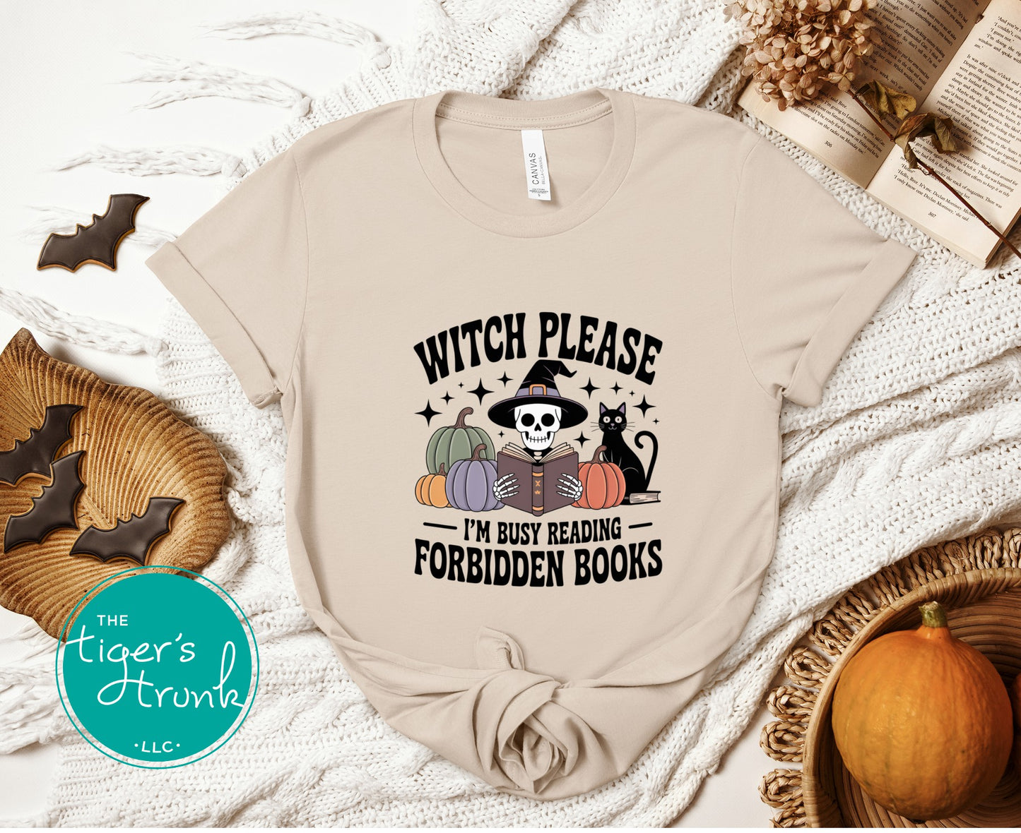 Beige t-shirt with Halloween-themed design featuring text and graphics, placed on a textured surface with decorative items.