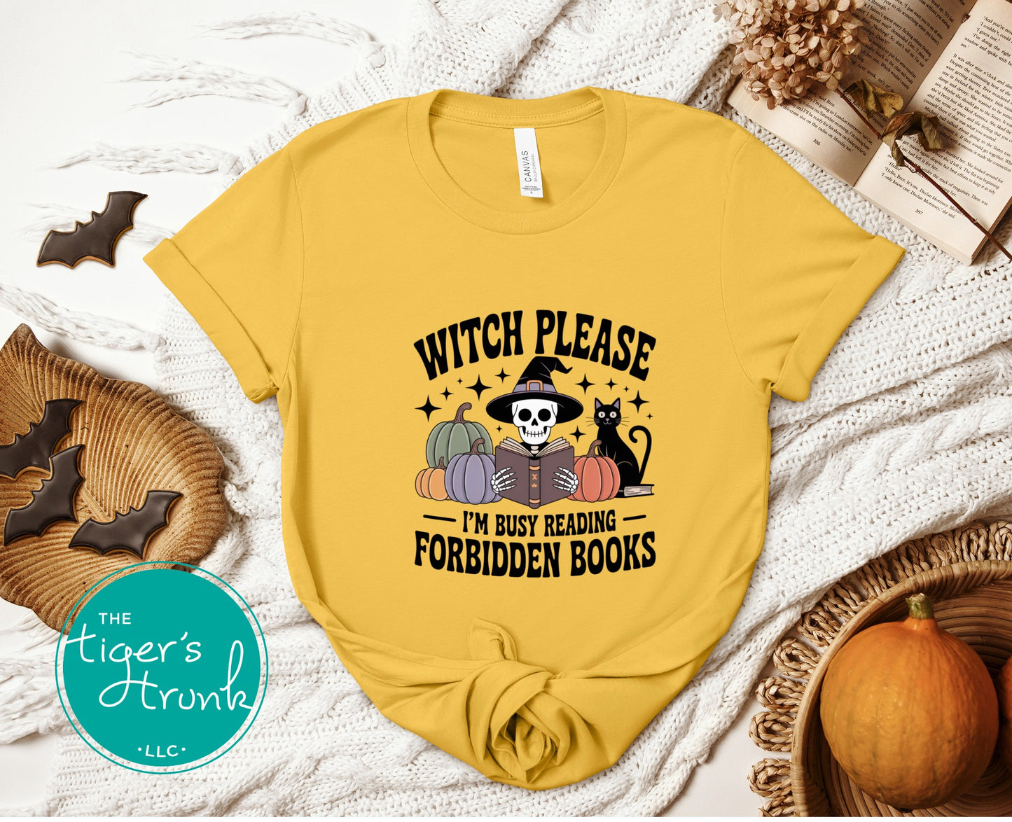 Yellow t-shirt with Halloween-themed design on a textured surface with pumpkins and cookies.