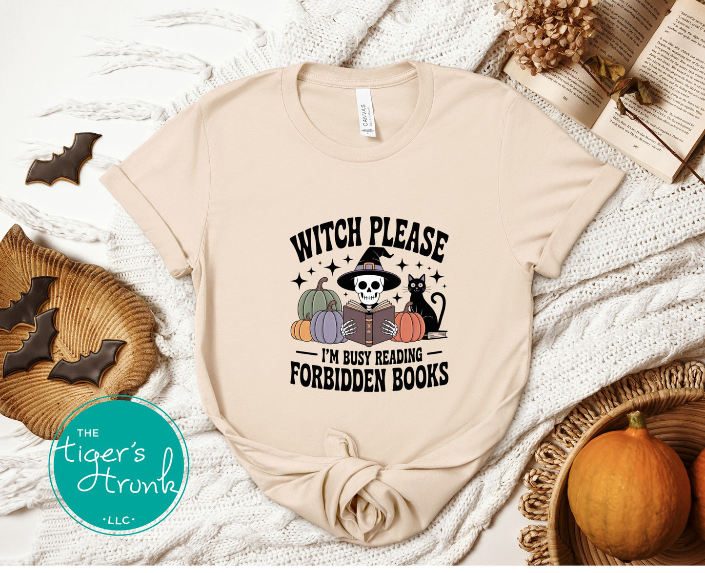 Beige t-shirt with Halloween-themed design on a textured surface with pumpkins and cookies.