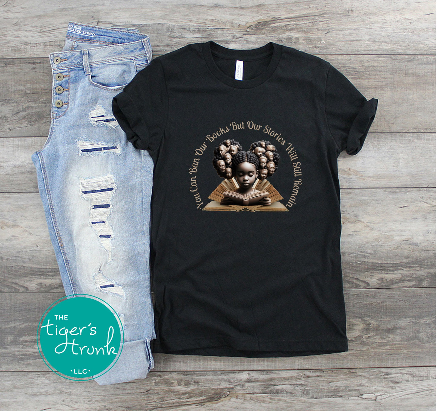 Black t-shirt with a graphic design and text on a wooden surface, next to jeans.
