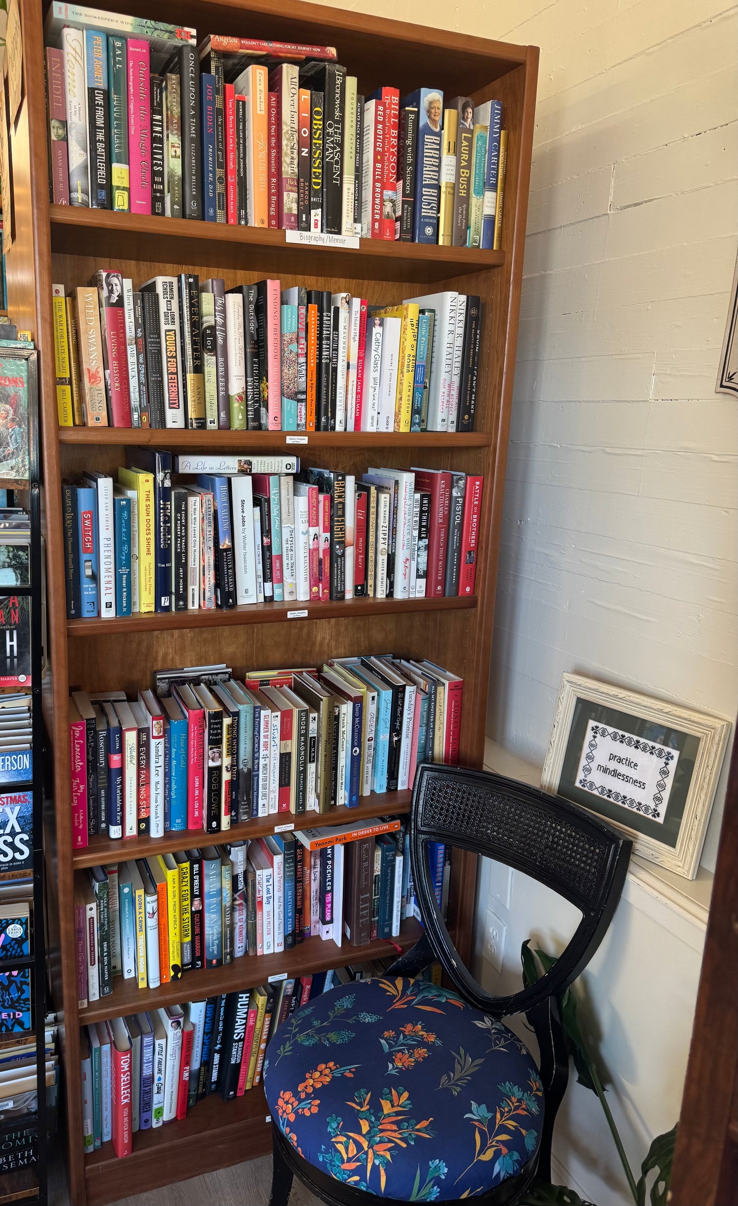 A thoughtfully arranged bookstore display featuring autobiography, biography, and memoir titles stacked beside a warm lamp, framed photos, and soft, inviting décor.