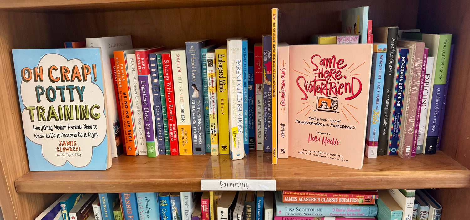 A warm bookstore display featuring parenting and family nonfiction books arranged beside a cozy mug, a framed family quote, and soft, homey décor in gentle lighting.