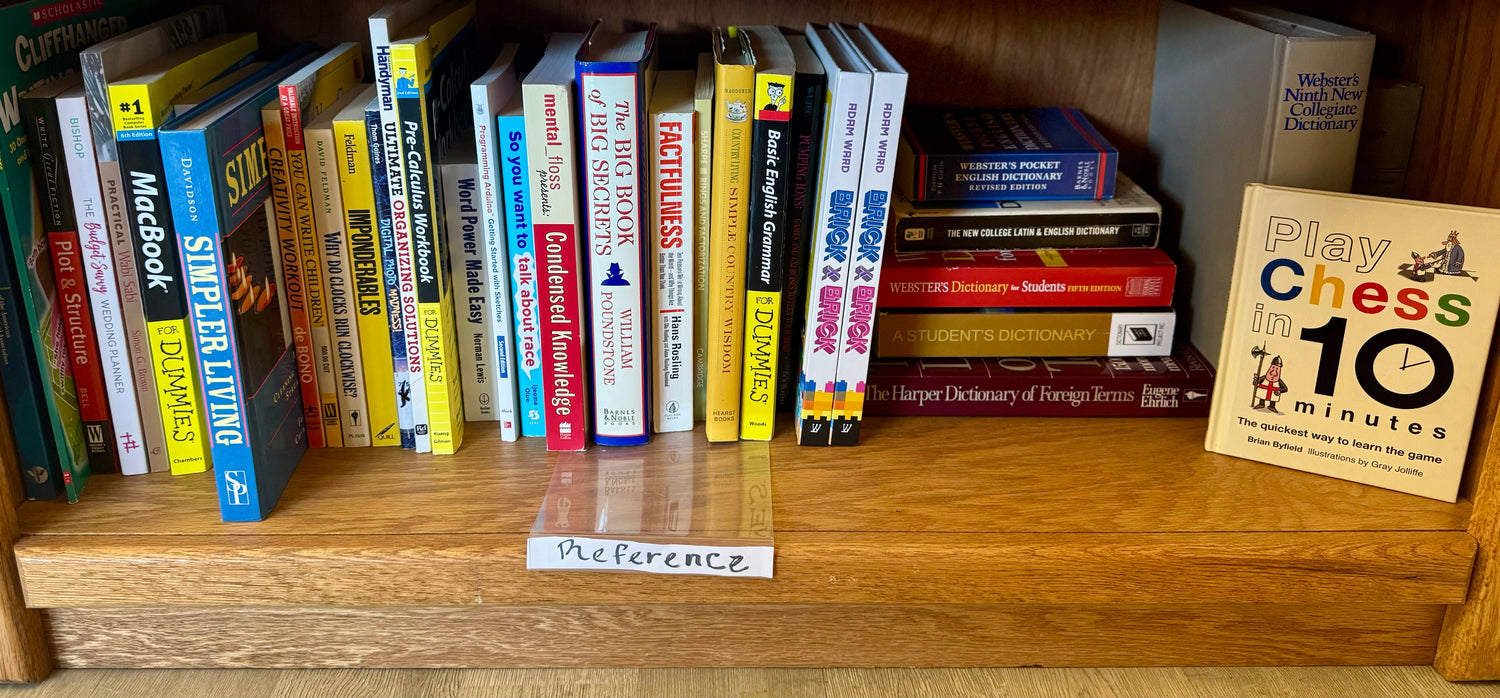 A tidy bookstore display featuring reference books such as dictionaries, handbooks, and guides arranged neatly beside a notebook and a small desk lamp.