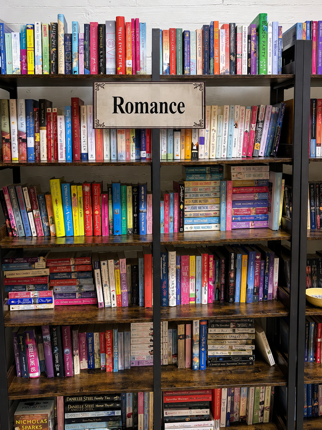 A cozy bookstore table display featuring romance novels, a vase of roses, candles, and warm lighting with pink and red accents for a romantic feel.