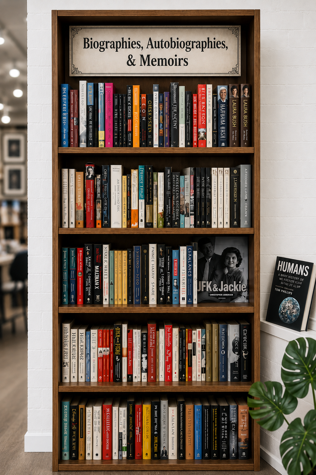A thoughtfully arranged bookstore display featuring autobiography, biography, and memoir titles stacked beside a warm lamp, framed photos, and soft, inviting décor.