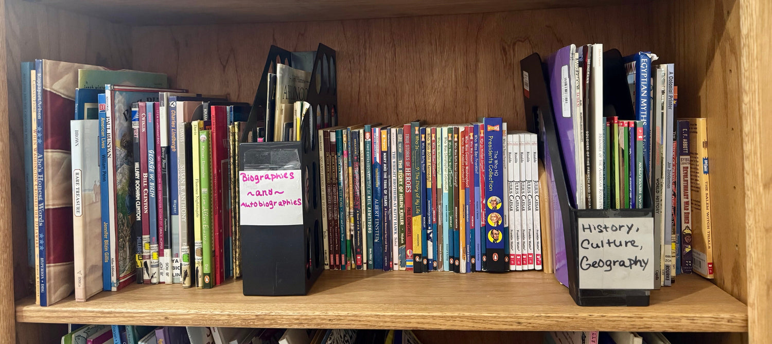 A colorful bookstore display featuring children’s history and biography books arranged with small world-history props, a globe, and bright classroom-style décor.
