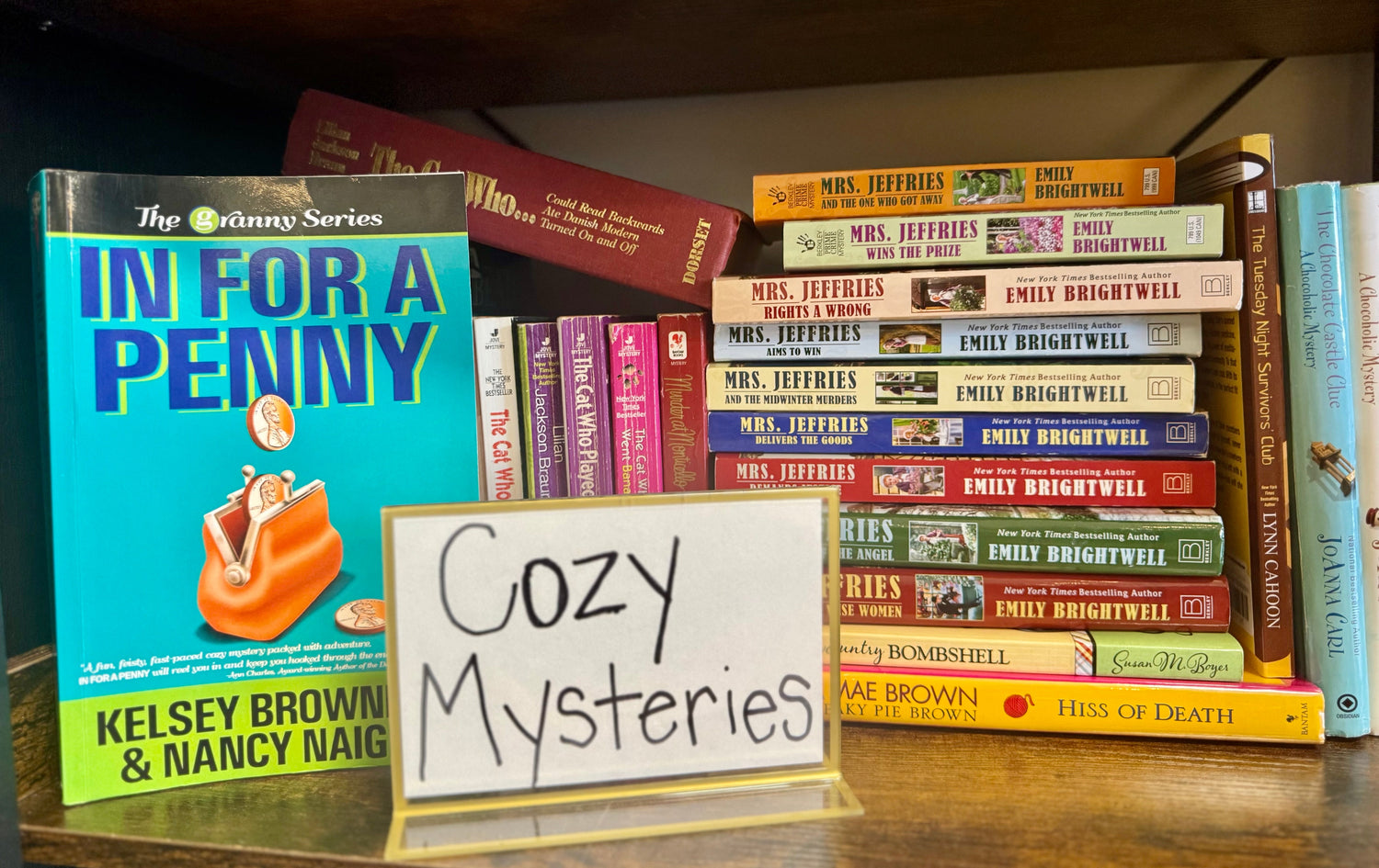 A warm bookstore display featuring cozy mystery novels, a teacup, knitted throw blanket, and soft lighting for a comfortable, inviting atmosphere.