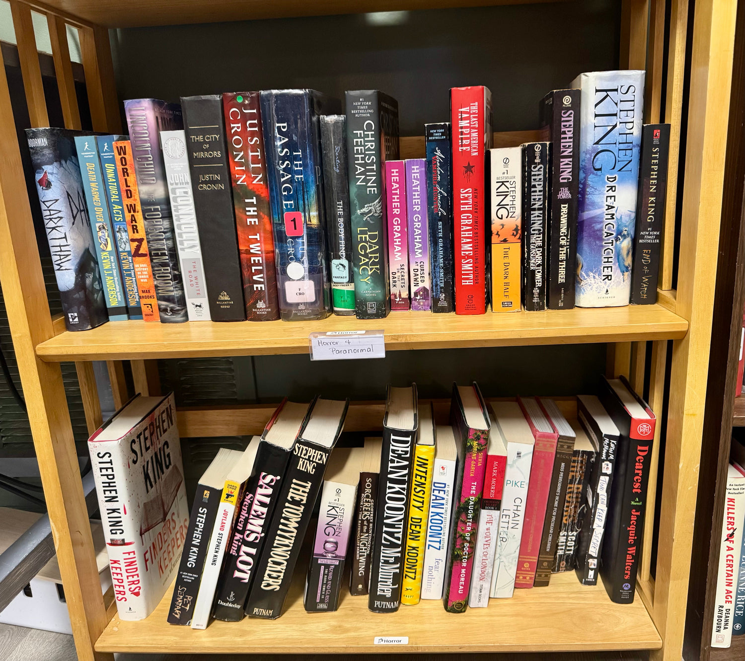 A dark, moody bookstore display featuring horror and paranormal mystery novels surrounded by candles, skull décor, and subtle fog or shadowy lighting.