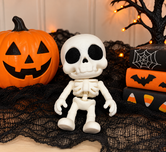 Cute 2.5-inch white 3D printed articulated skeleton fidget toy with oversized skull, black eyes, and movable limbs, displayed beside an orange jack-o'-lantern and Halloween decorations.