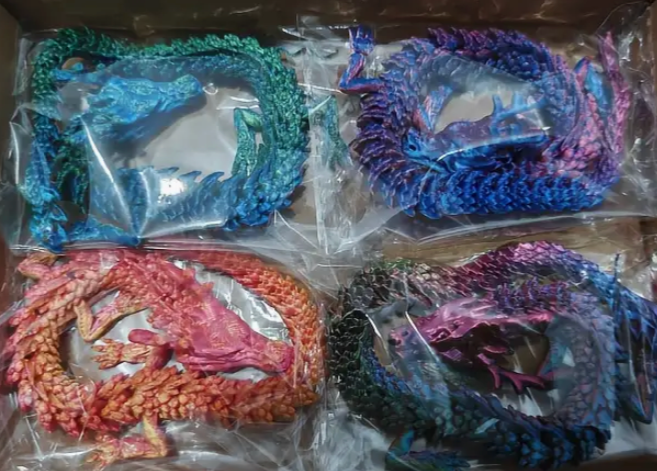 Four colorful dragon figurines in clear packaging on a cardboard surface.