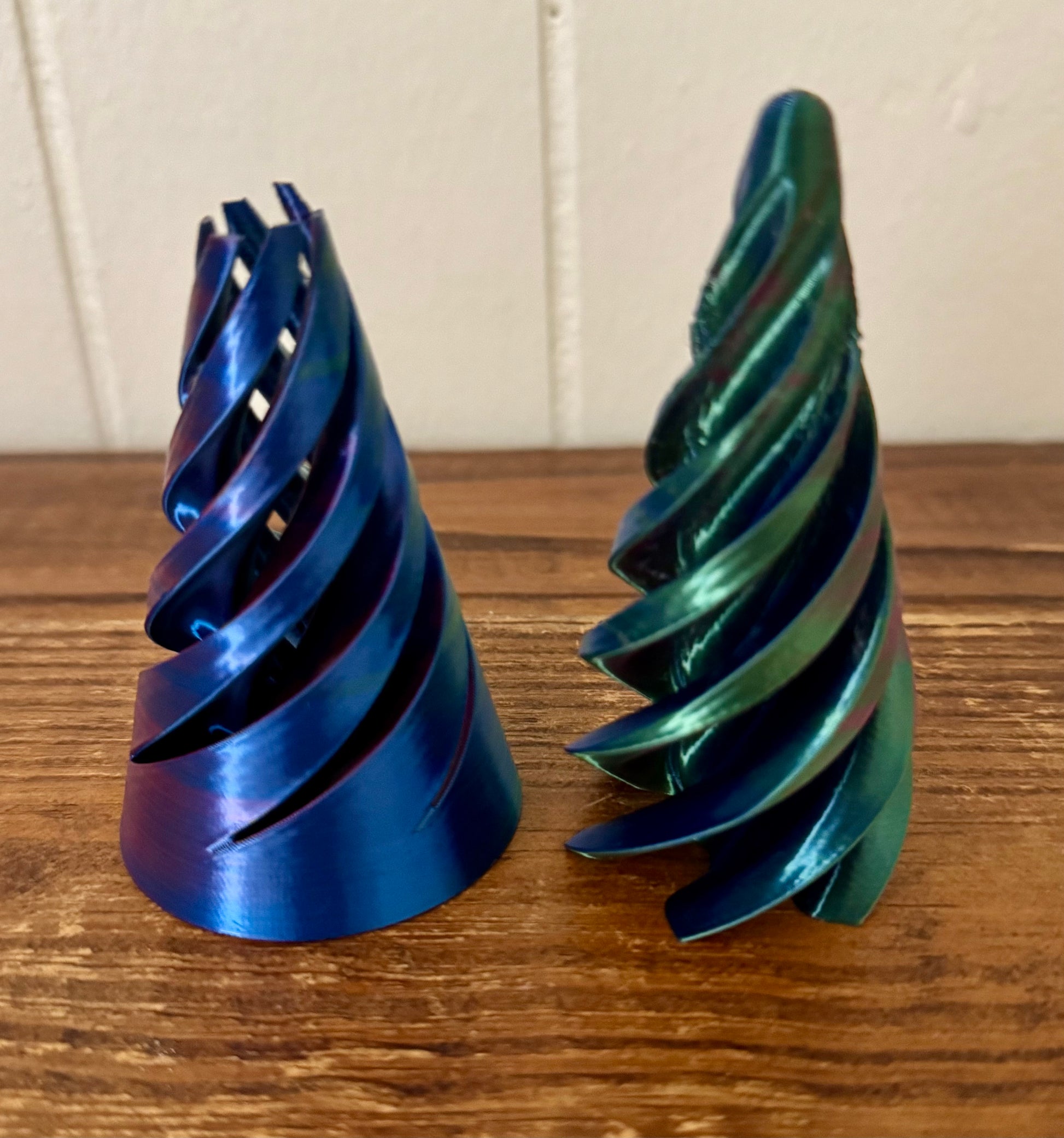 Two metallic spiral-shaped objects on a wooden surface with a white paneled wall background.