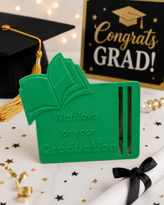 green 3D printed graduation money holder with graduation book design and congratulatory message displayed beside graduation cap and diploma decor