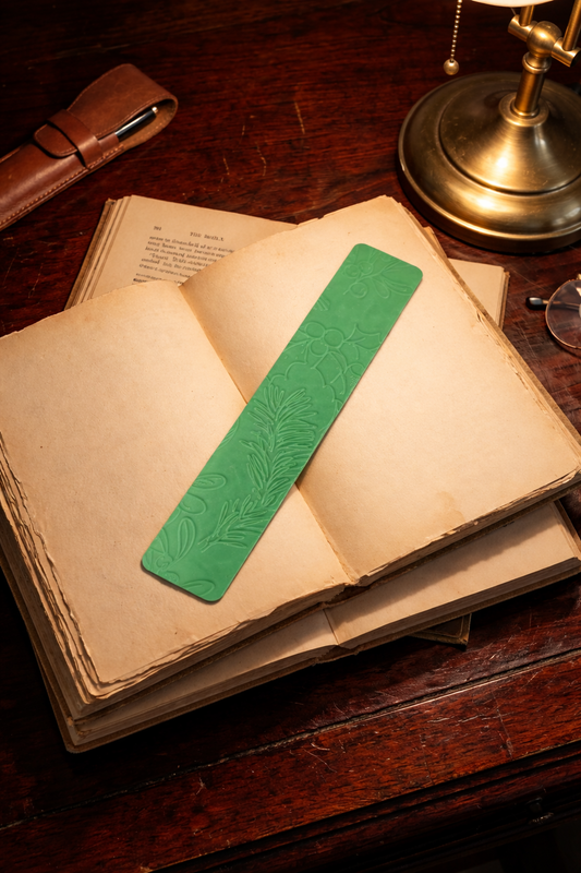 3D printed green botanical bookmark with embossed design resting on an open vintage book on a wooden desk