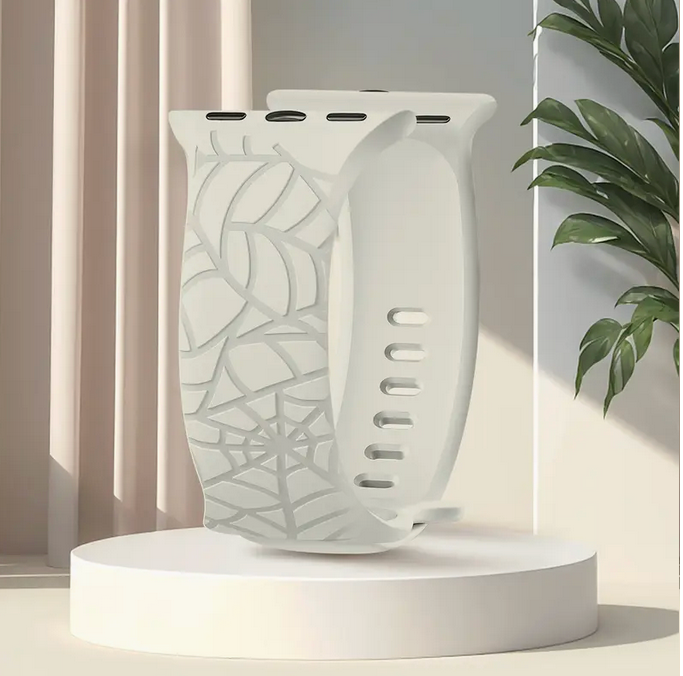 Decorative apple watch band with spider web pattern on a white pedestal against a neutral background