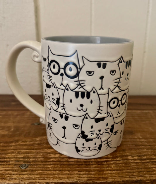 Ceramic mug with black and white illustrated cat faces and a unique curled handle on a wooden surface