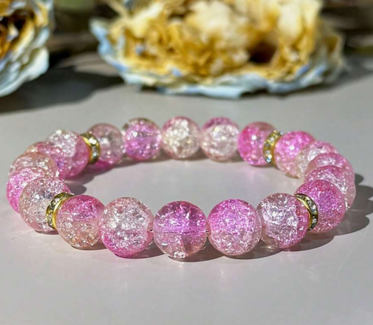 Pink beaded bracelet with gold accents on a light surface
