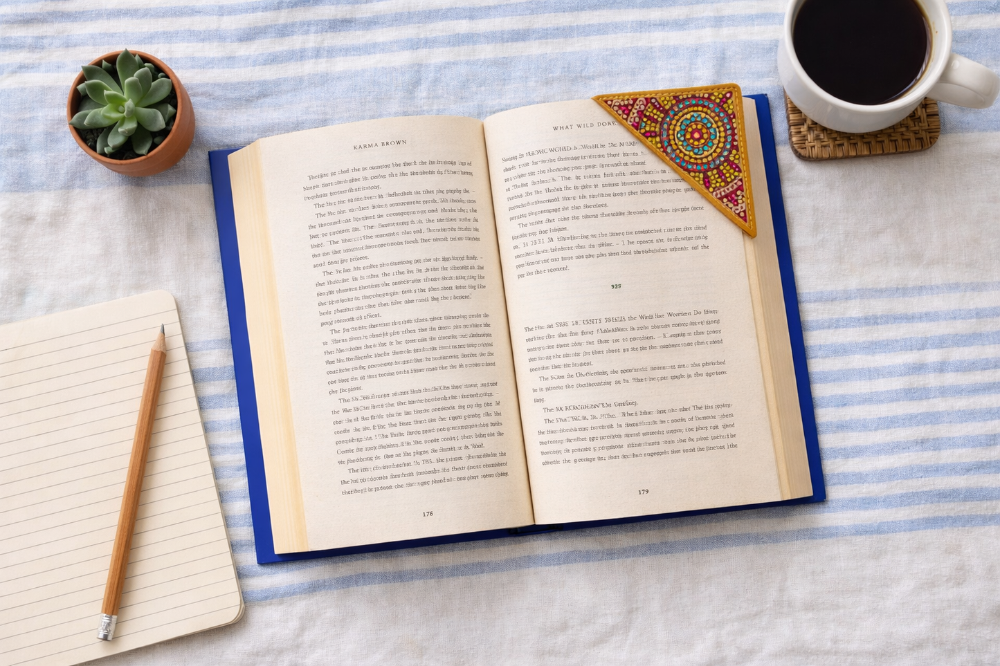 Open book on blue striped fabric with coffee and bejeweled vegan leather corner bookmark for cozy reading