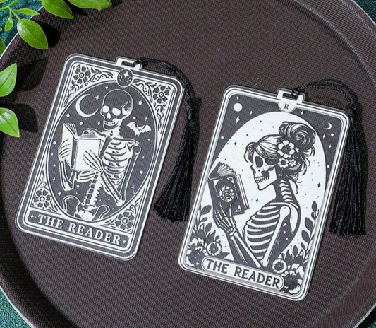 Two skeleton-themed bookmarks labeled 'The Reader' on a dark surface with green leaves.