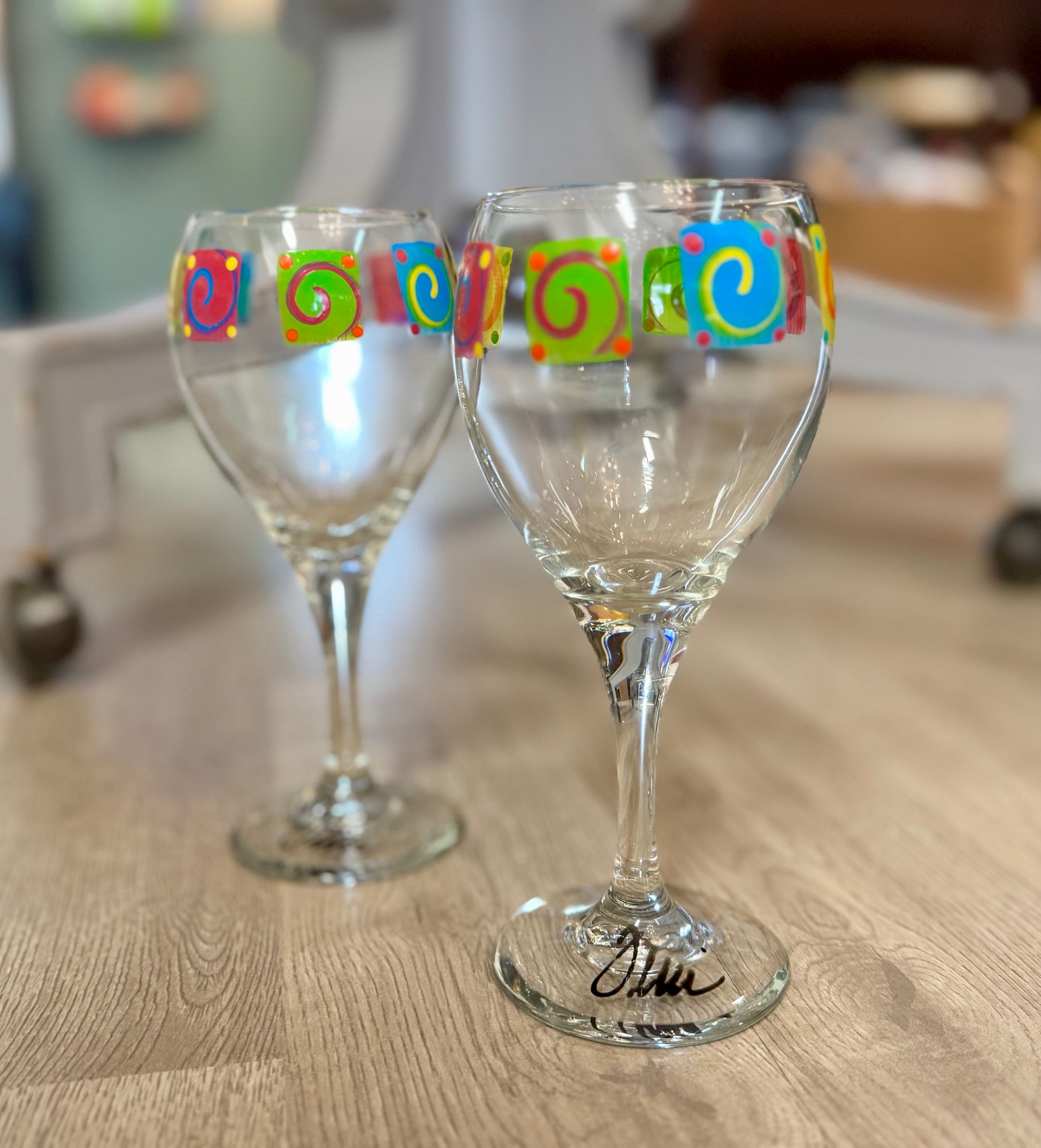 Pair of hand-painted wine glasses featuring colorful swirl square designs and signed glass bases