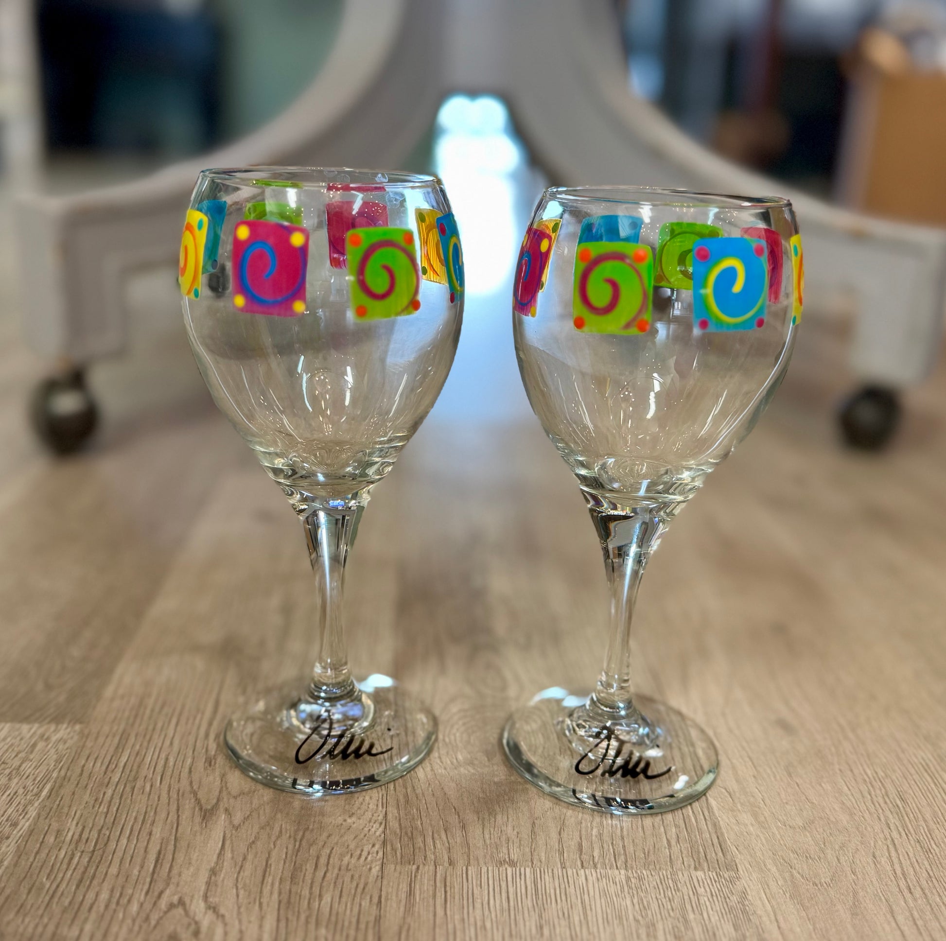 Pair of hand-painted wine glasses featuring colorful swirl square designs and signed glass bases