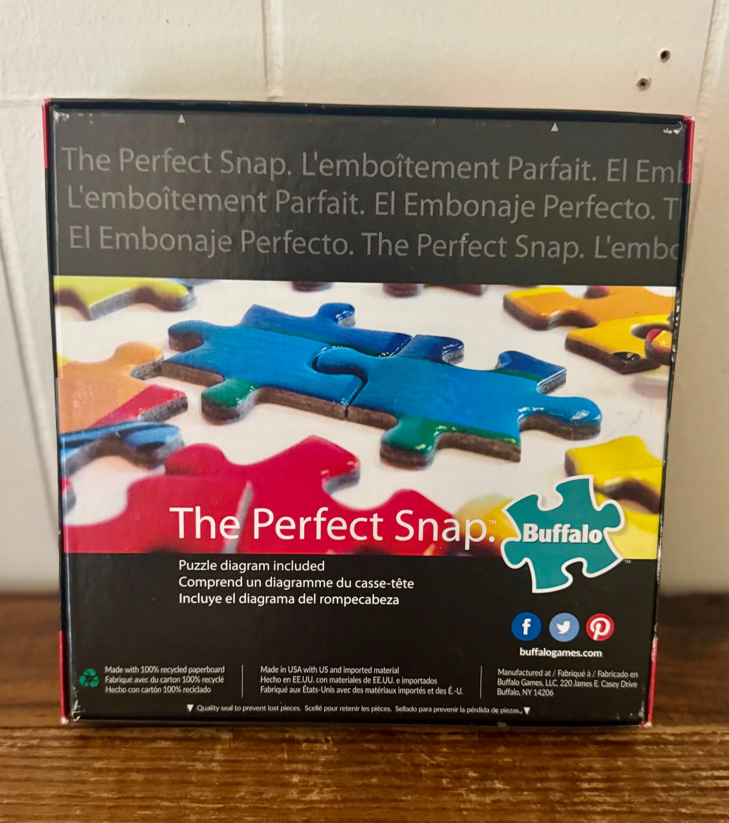 Box of Buffalo Games 'The Perfect Snap' puzzle with colorful jigsaw pieces on a wooden surface.