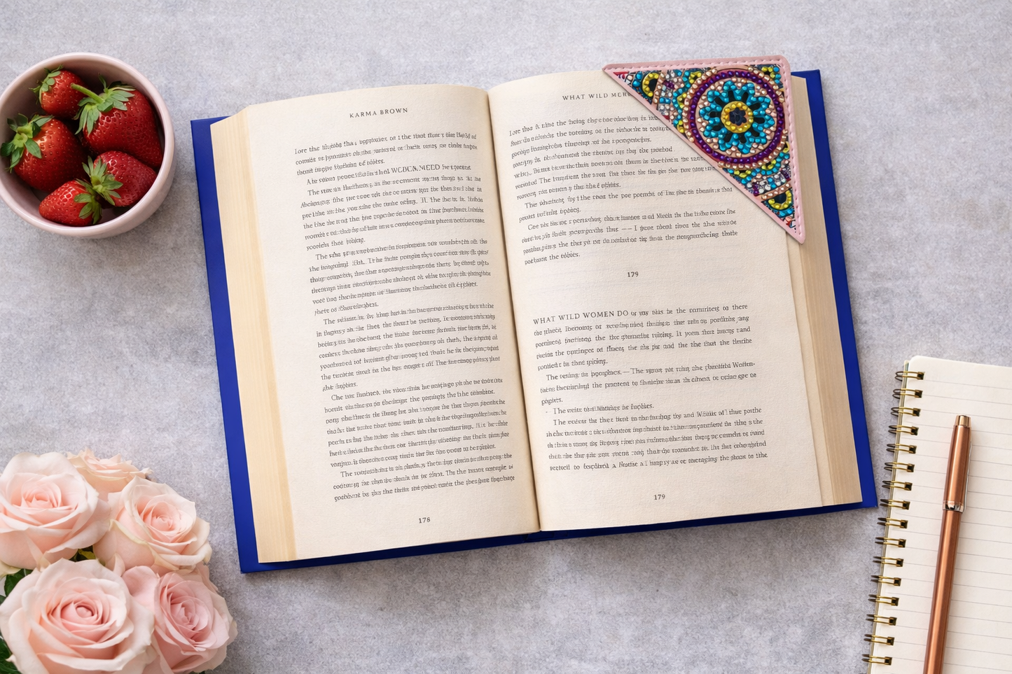 Open book styled with roses, notebook, and colorful bejeweled vegan leather corner bookmark on soft background