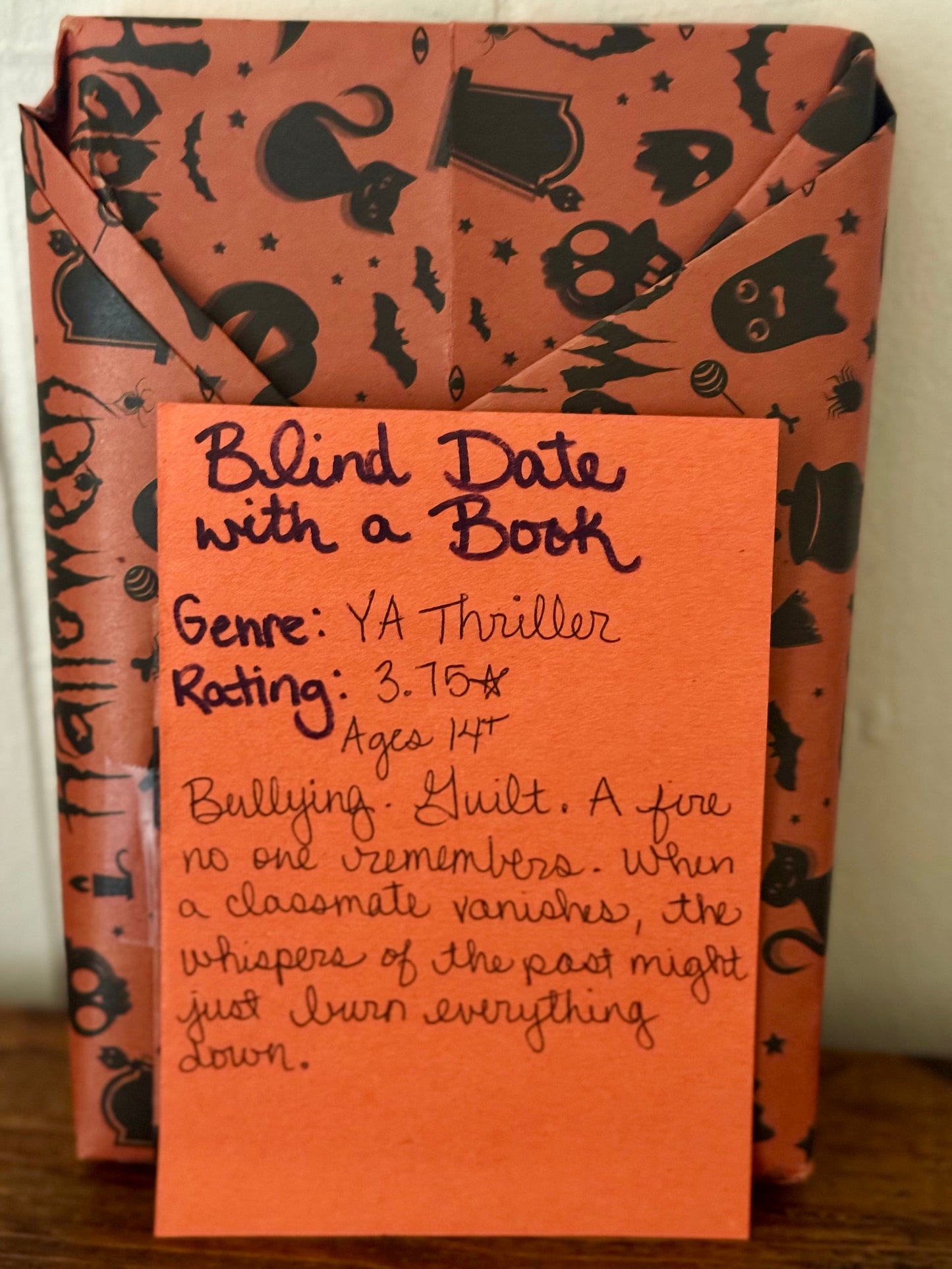 Book with Halloween-themed cover and a descriptive card on a wooden surface