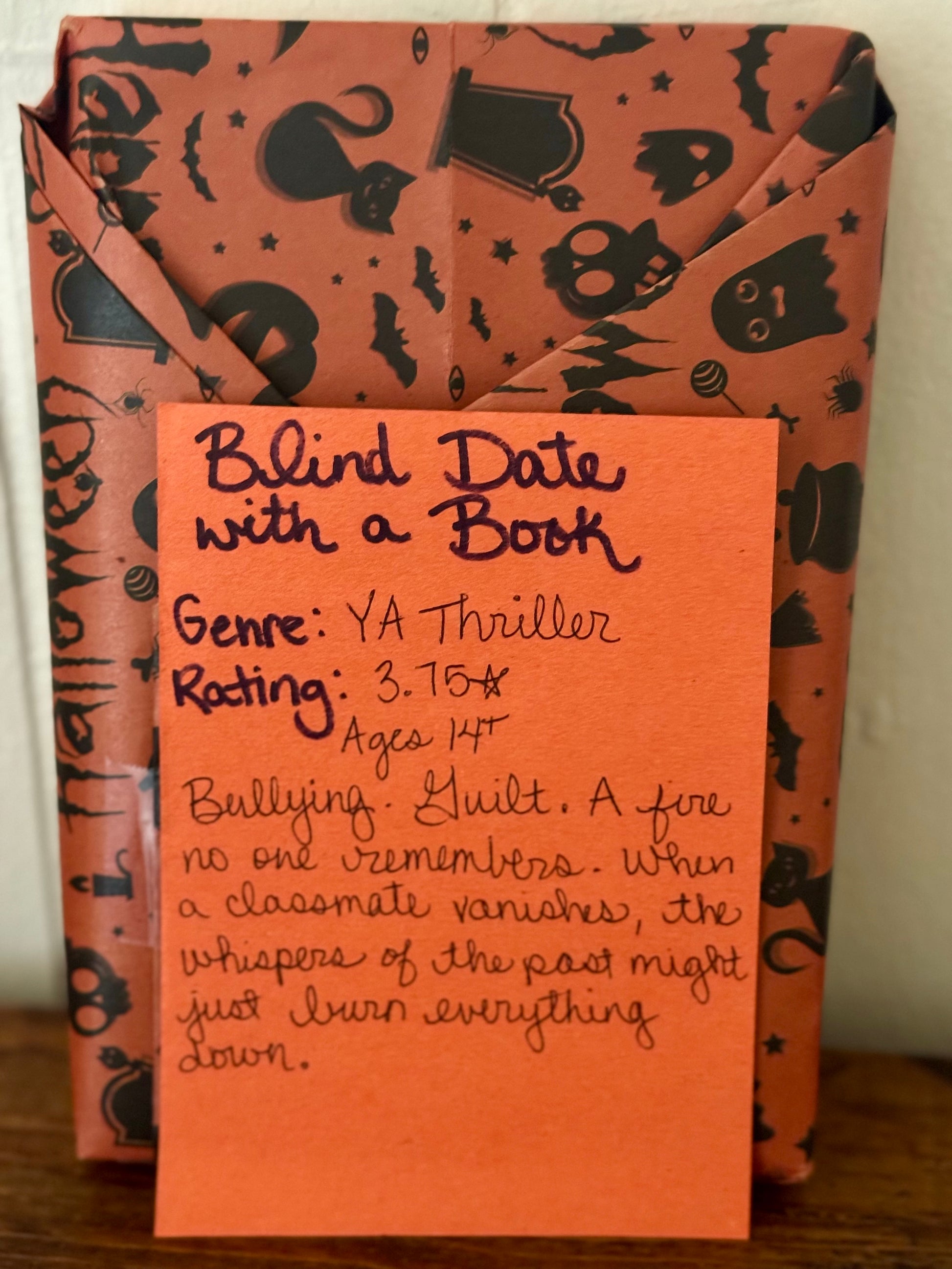 Book with Halloween-themed cover and a descriptive card on a wooden surface