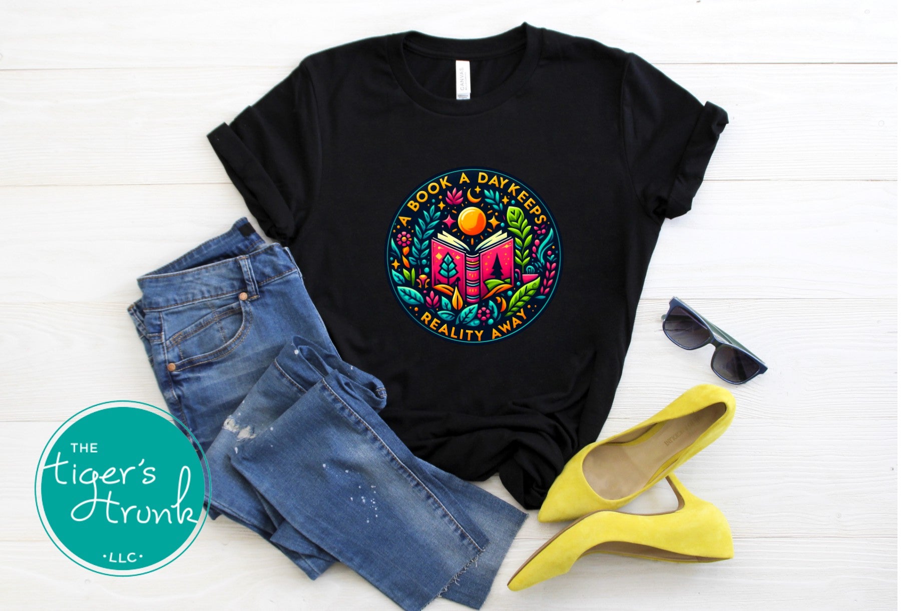 Black t-shirt with colorful graphic design, blue jeans, yellow shoes, and sunglasses on a white background.