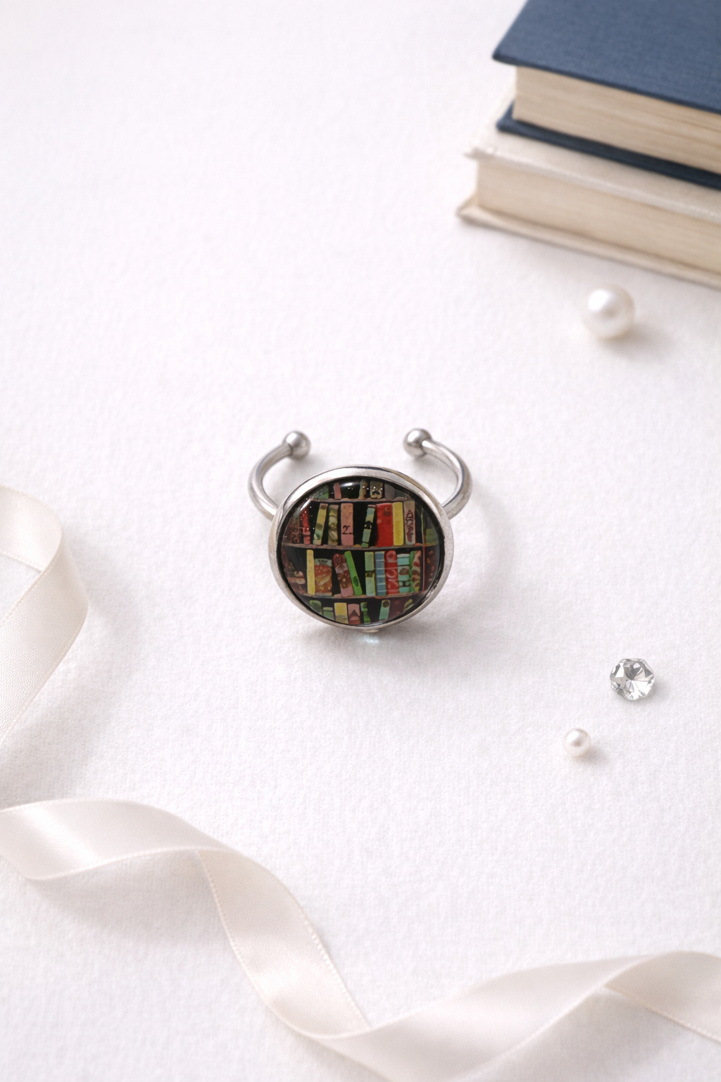 Adjustable book lover ring featuring a colorful bookshelf design. Silver tone adjustable band with glass cabochon, perfect for readers, librarians, and bookworms.