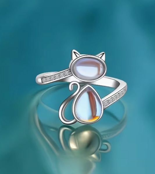 Adjustable silver tone cat ring with opal glass stones and open wrap design photographed on a teal background