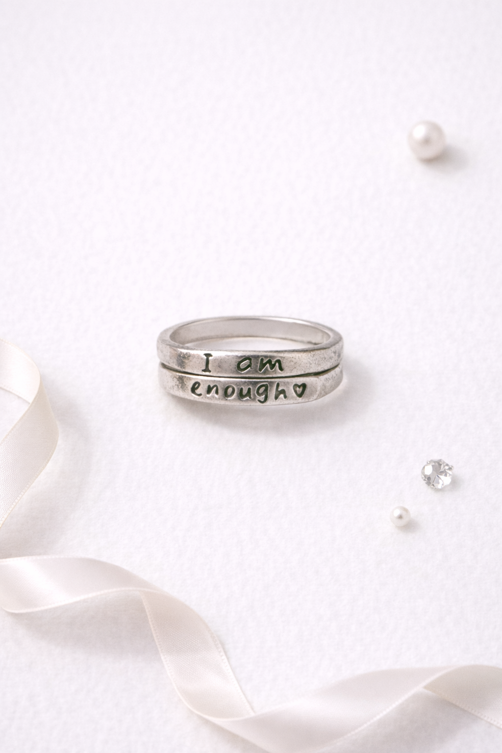 Adjustable silver tone affirmation ring engraved with the message I am enough displayed on a soft neutral flatlay background with ribbon and accent details