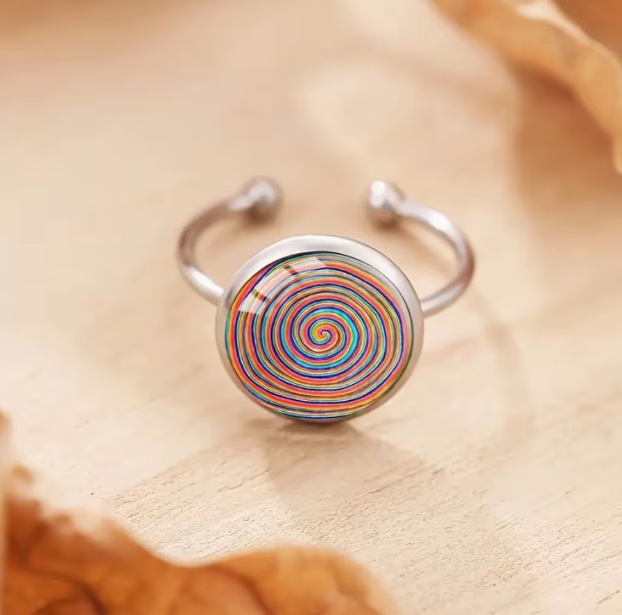 Adjustable silver tone ring featuring a round glass cabochon with a vibrant multicolor spiral swirl design displayed on a wooden surface.