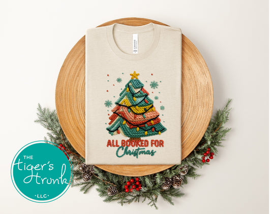 Natural heather short-sleeve shirt featuring a cozy knitted Christmas tree design with "All Booked for Christmas."