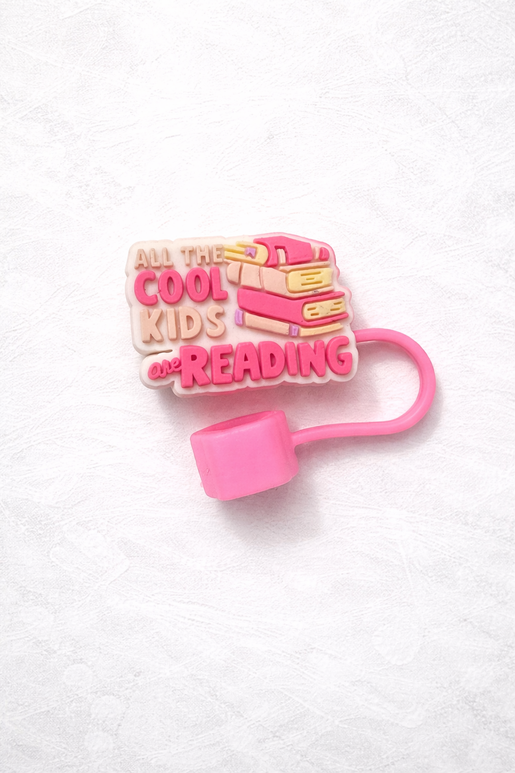 Pink silicone straw topper with stacked books and the phrase All the Cool Kids Are Reading, attached to a flexible loop for reusable tumbler straw.