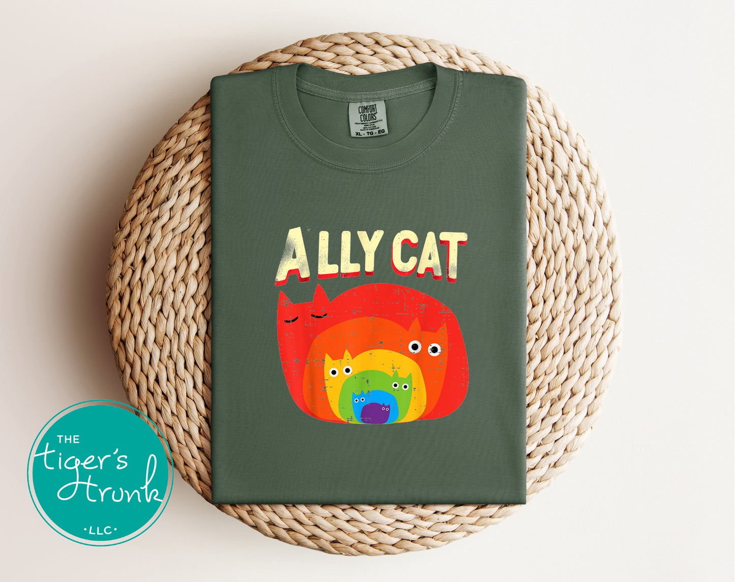 Comfort Colors moss green Ally Cat rainbow cat graphic t-shirt folded on woven mat flatlay